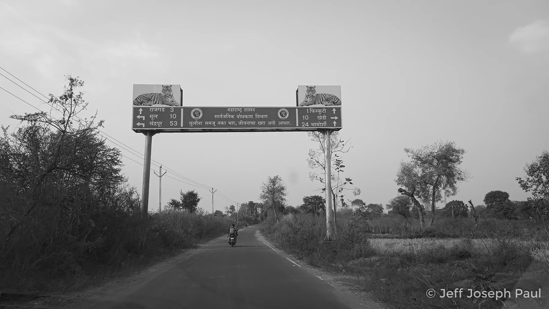 A motorcyclist passes direction signs at a road junction.